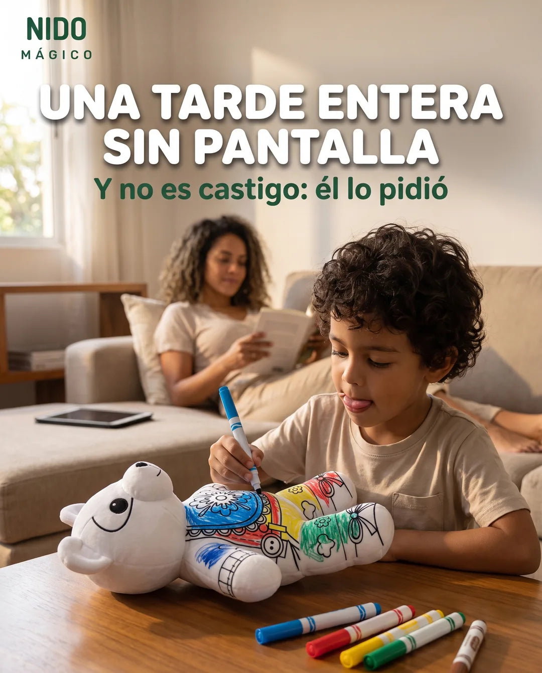 Niño concentrado coloreando su peluche de oso mientras su mamá lee en el sofá